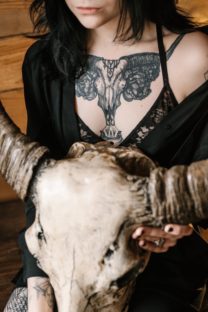 A stylish woman with tattoos holds a weathered steer skull indoors.