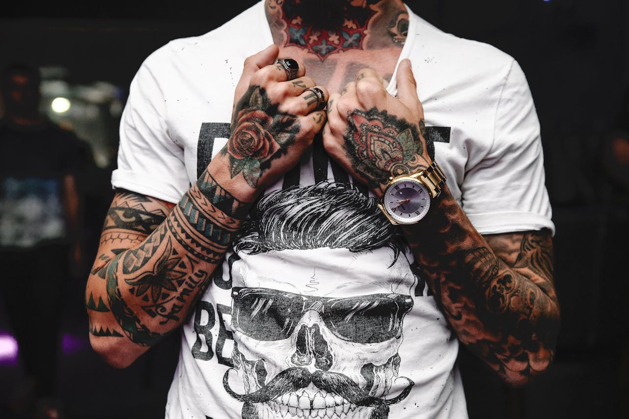Close-up of tattooed arms and hands clutching a graphic t-shirt featuring skull art.